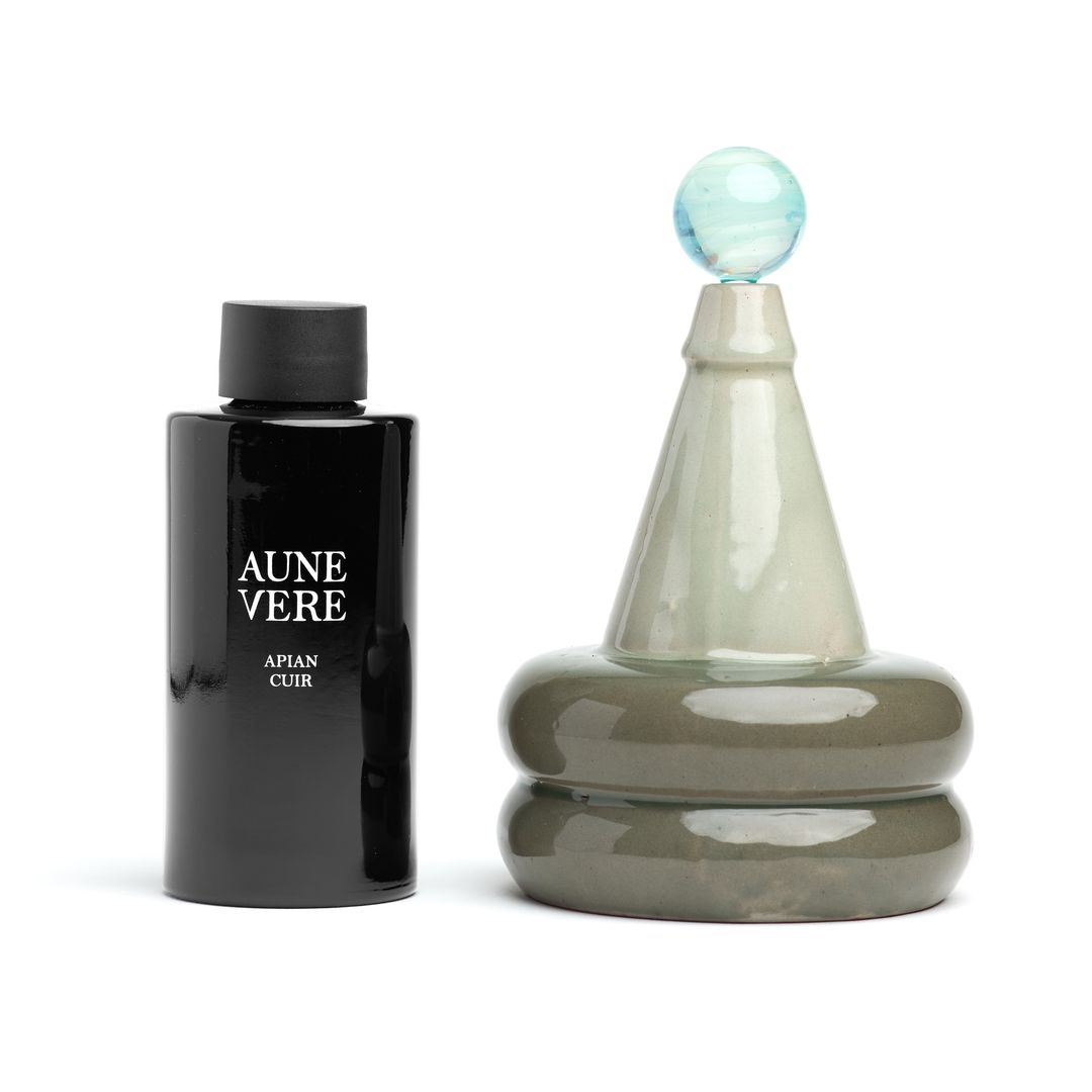 Apian Cuir 100 ml bottle beside the ceramic vessel, both on white.
