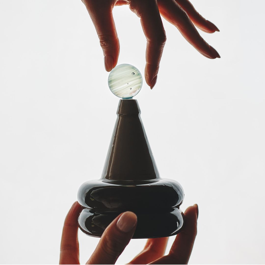 A hand turns the Apian Cuir vessel in daylight, thumb resting on the faceted glaze.