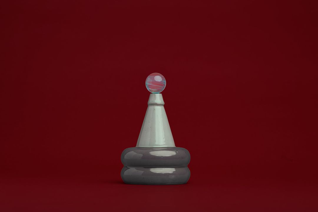 Apian Cuir ceramic vessel, a stacked glazed form holding a glass orb, on alder red paper.