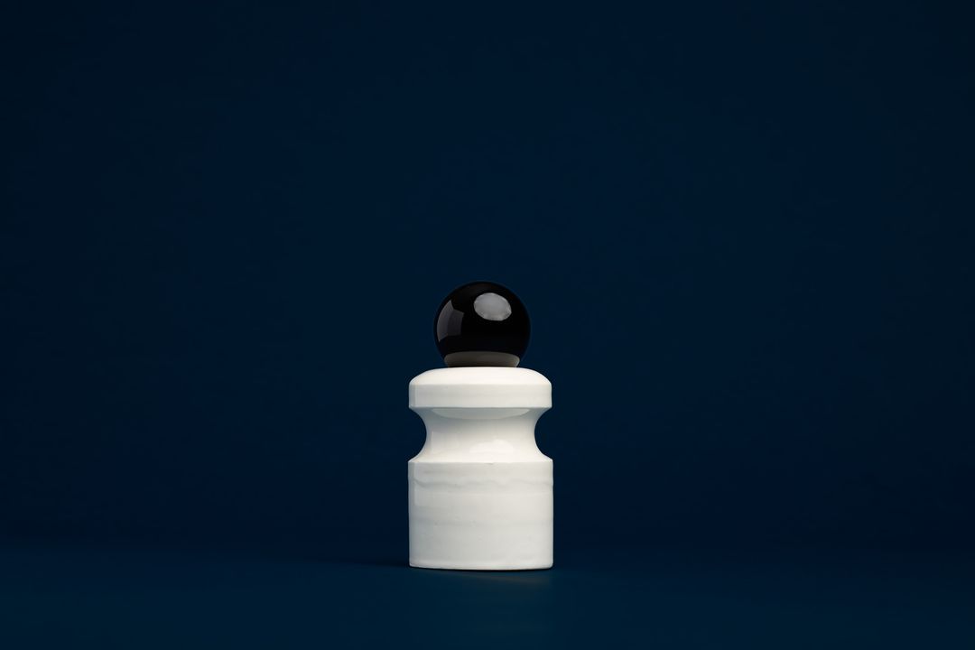 Caledonian Pear ceramic vessel, a faceted glazed base holding a clear glass orb, on deep navy paper.