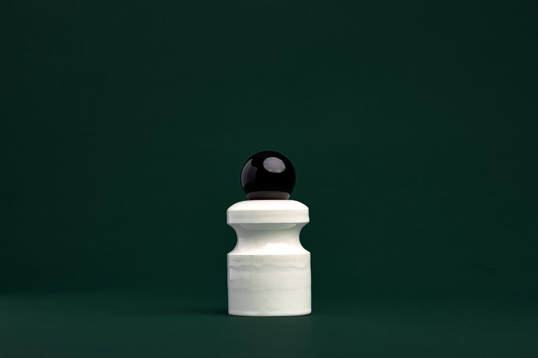 Caledonian Pear ceramic vessel, a faceted dark glazed base holding a clear glass orb, on mossy green paper.