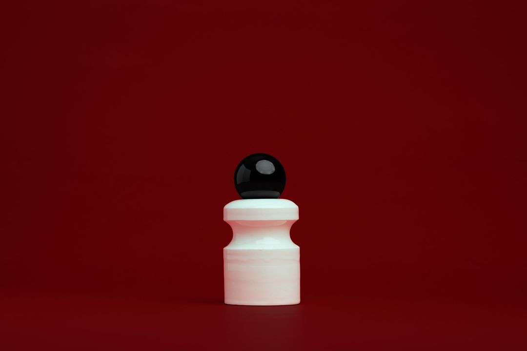 Caledonian Pear ceramic vessel, a faceted glazed base holding a clear glass orb, on alder red paper.