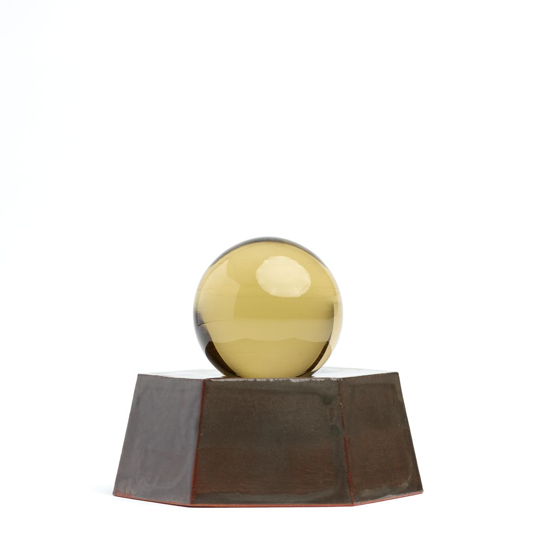 Eight Willow ceramic vessel on white, a faceted brown glazed base holding an amber glass orb.