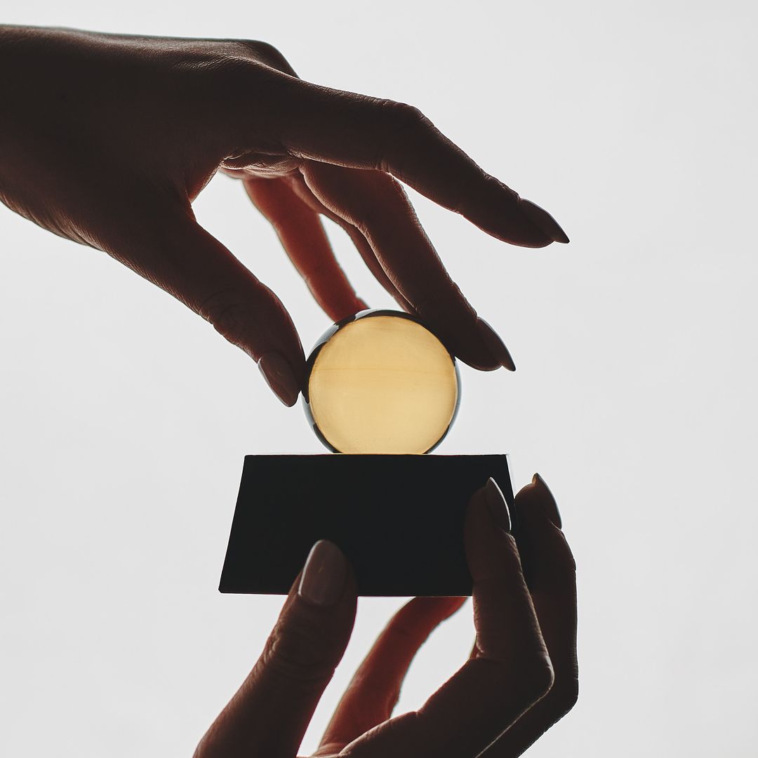 A hand lowers the clear glass orb back onto the Eight Willow ceramic vessel, fingers spread to steady it.