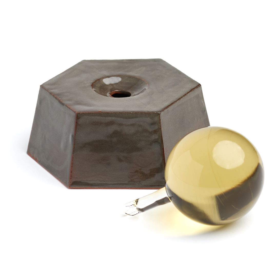 The open Eight Willow ceramic base beside its amber borosilicate glass applicator, on white.
