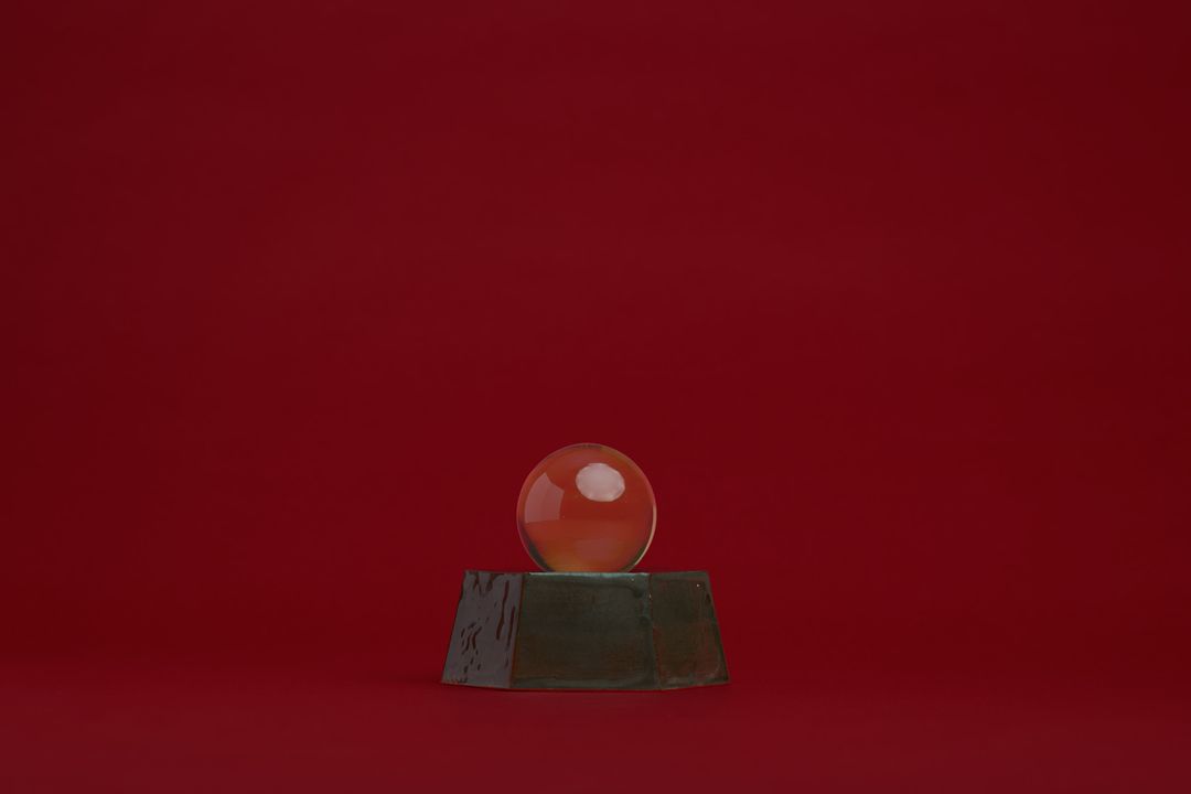 Eight Willow ceramic vessel, a faceted dark glazed base holding a clear glass orb, on alder red paper.