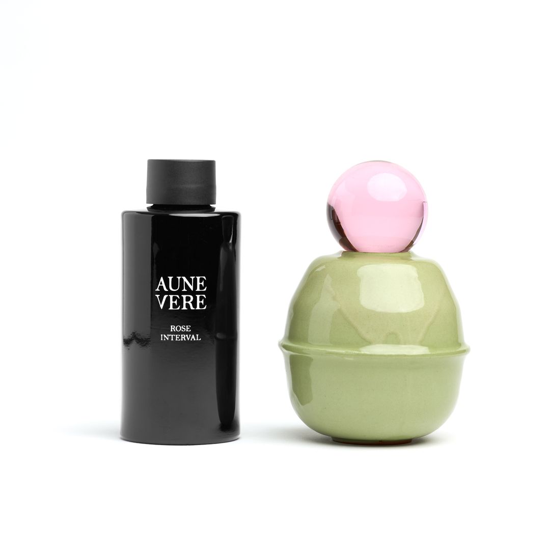 Rose Interval 100 ml bottle beside the ceramic vessel, both on white.