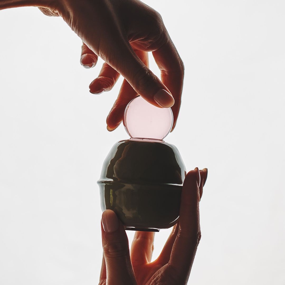 A hand cradles the Rose Interval vessel in daylight, the glass orb catching the light above the glazed base.