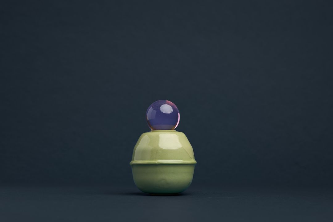 Rose Interval ceramic vessel, a pale green glazed form holding a glass orb, on deep navy paper.